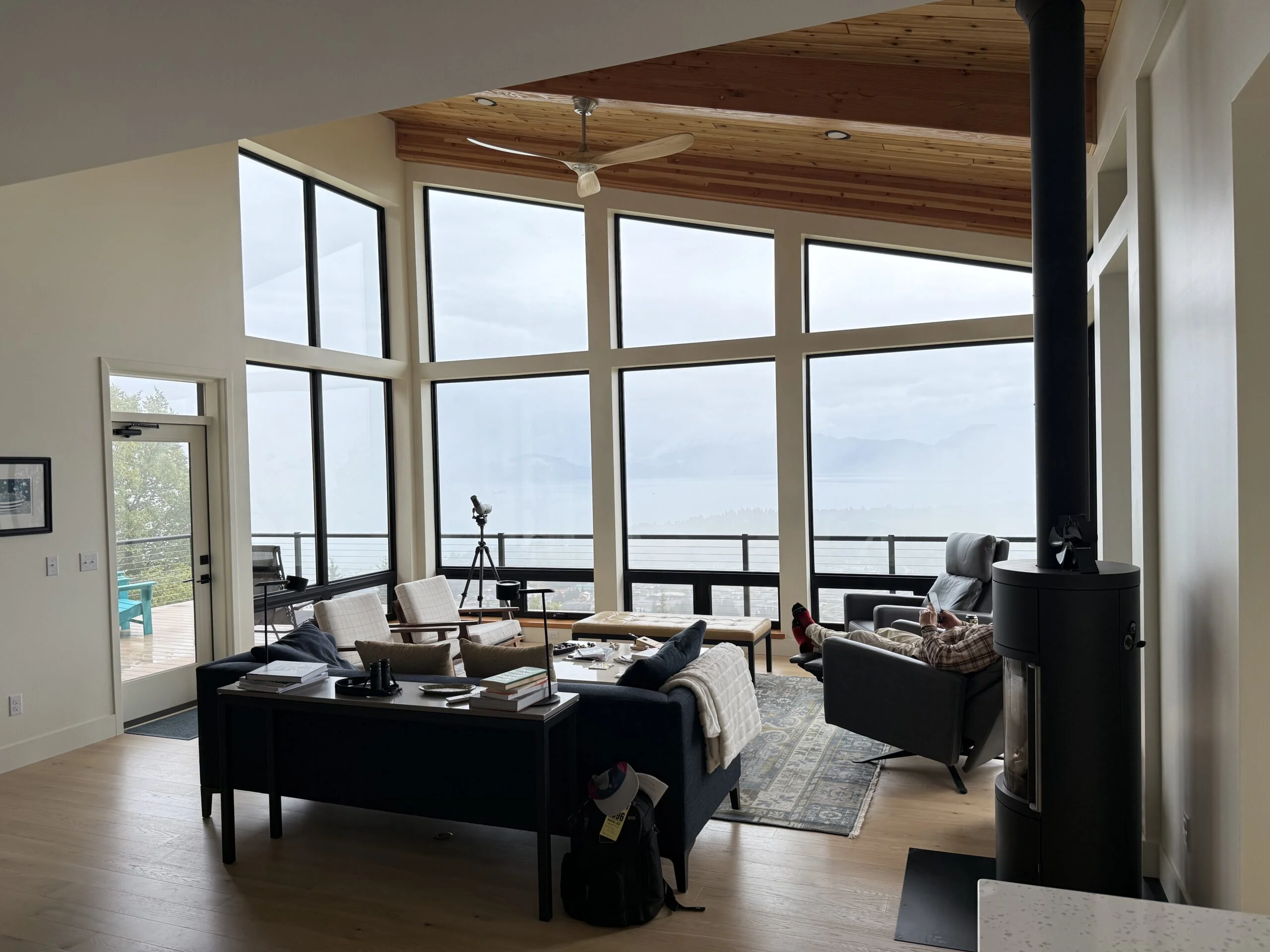 Home With a View — A hilltop Homer residence that takes full advantage of Kachemak Bay ocean views — post-and-beam structure with a full-width window wall framing the bay and the Kenai Mountains beyond.